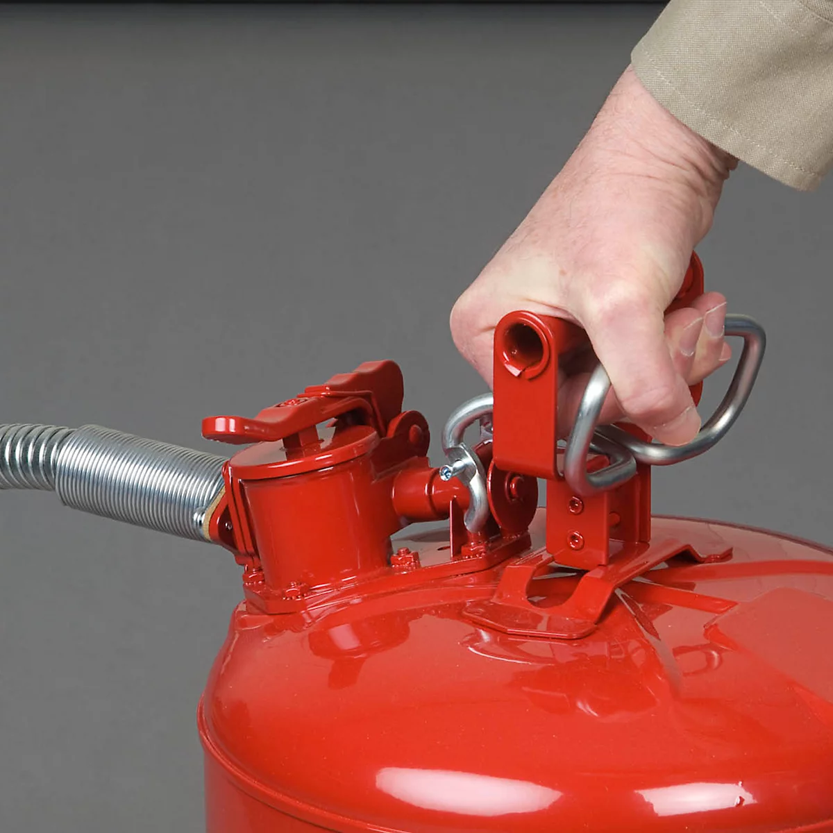 Close-up of red gas can top, handle in hand. Gray background in the background.