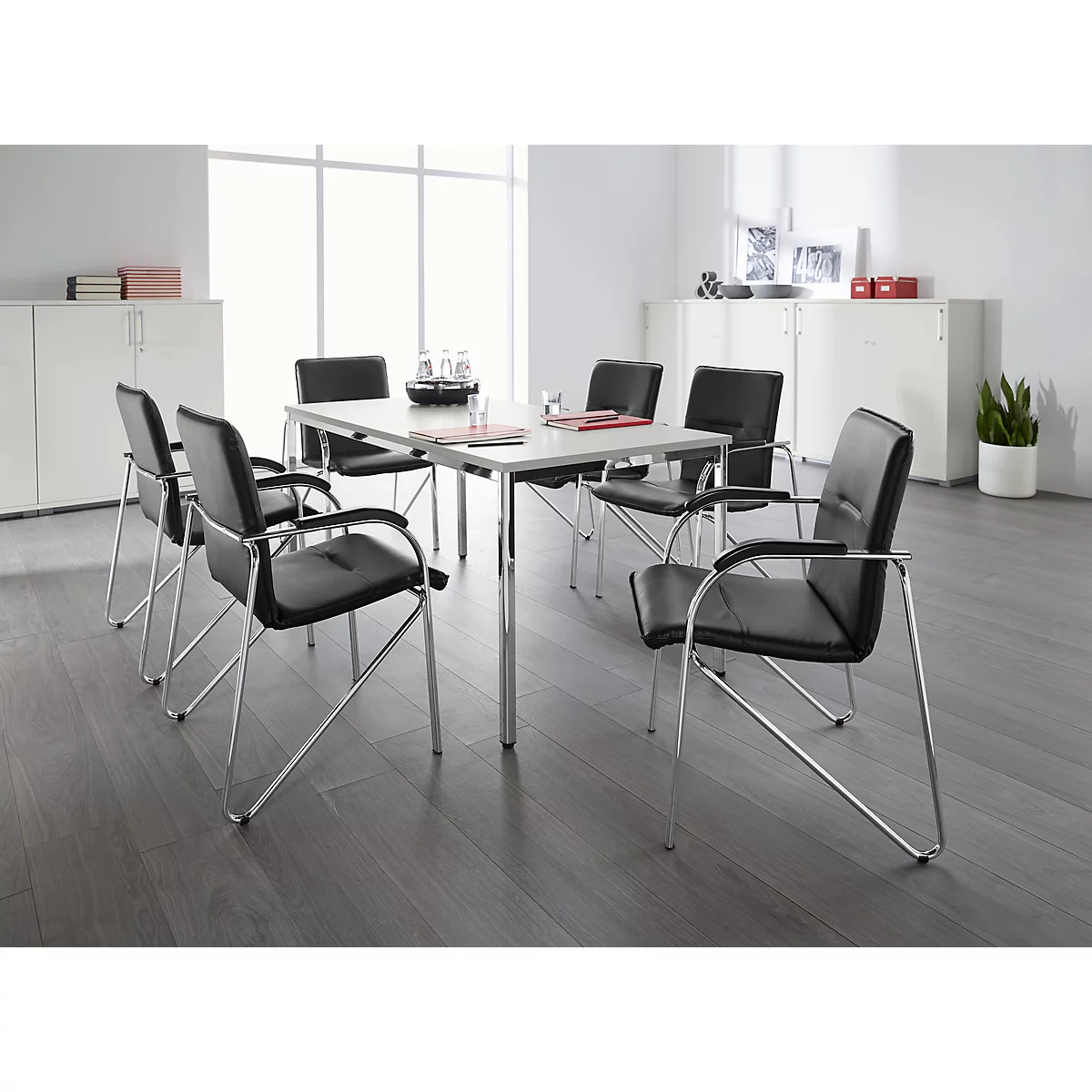 Een vergadertafel met zwarte stoelen in een lichte ruimte. Papier en een karaf liggen op de tafel.
