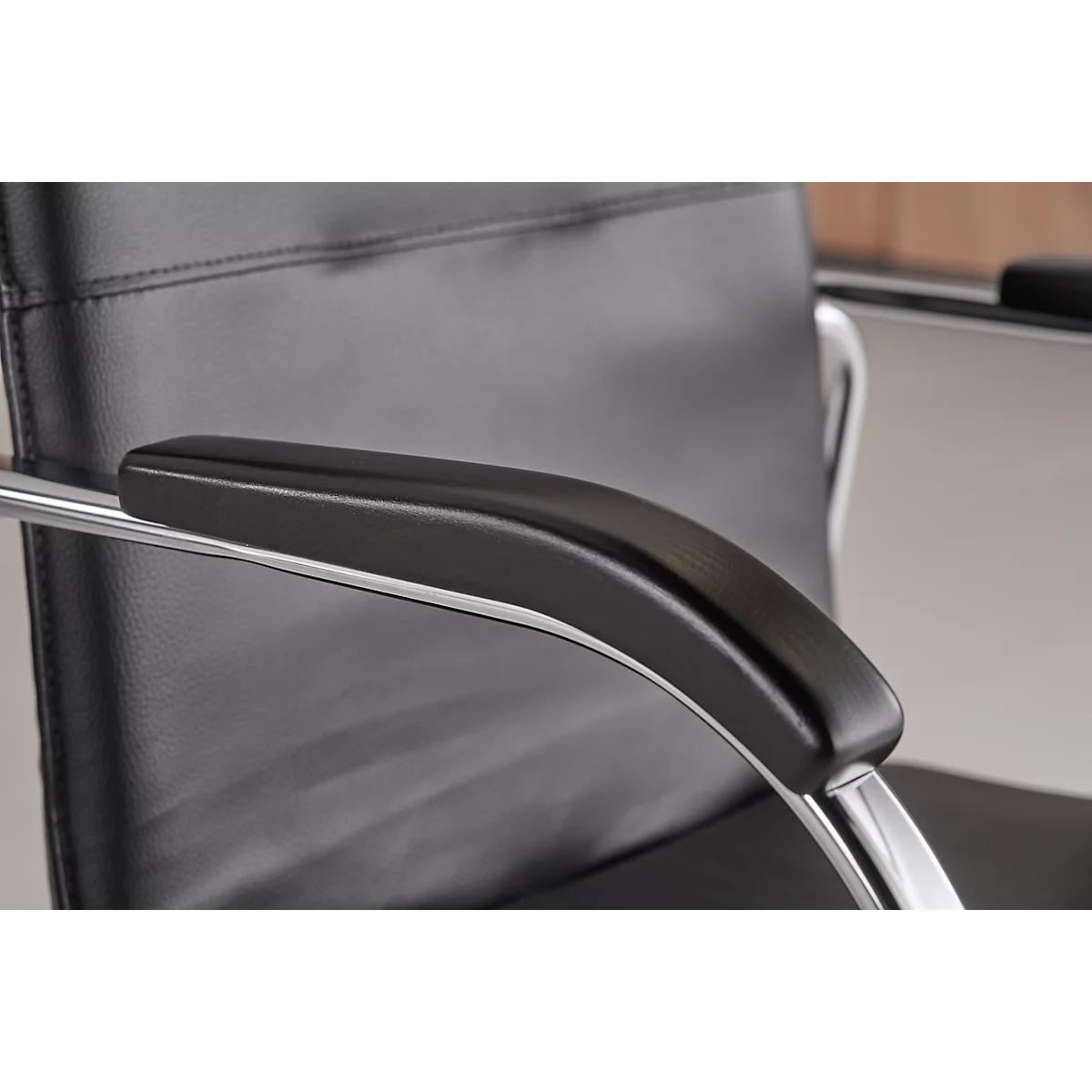 Close-up of an office chair armrest. Black, padded armrest on chrome metal.