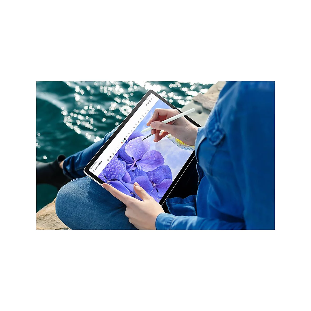 Person zeichnet auf Tablet mit Stift, im Hintergrund Wasser und blaue Hortensien.