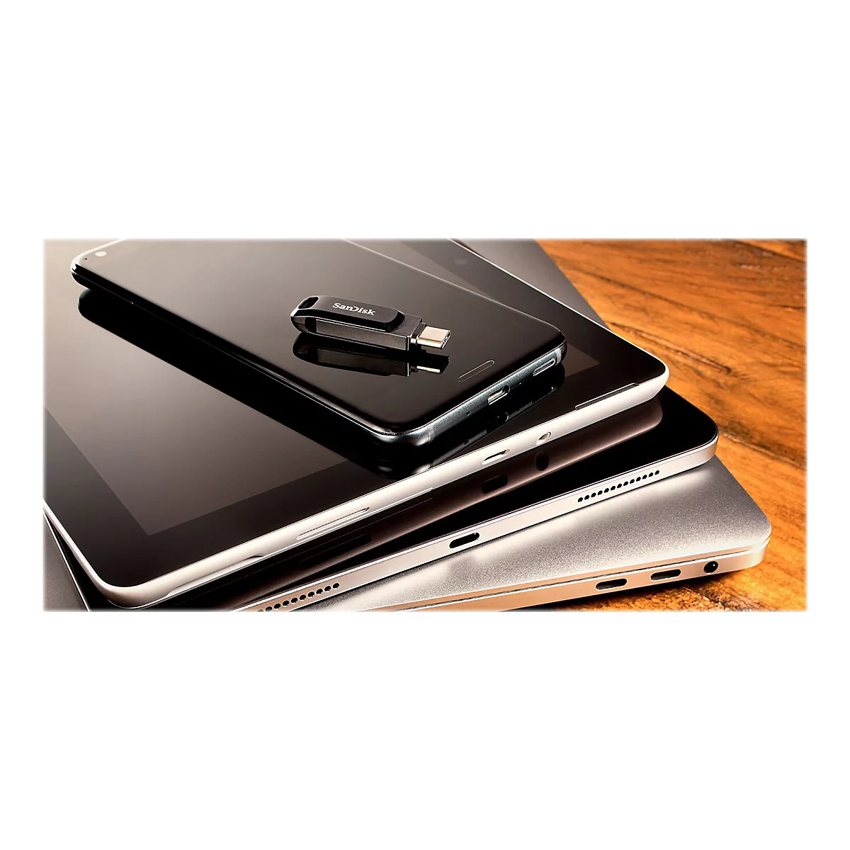 Schwarzes Smartphone, Tablet und Laptop übereinander. Darauf ein USB-Stick mit SanDisk-Logo.