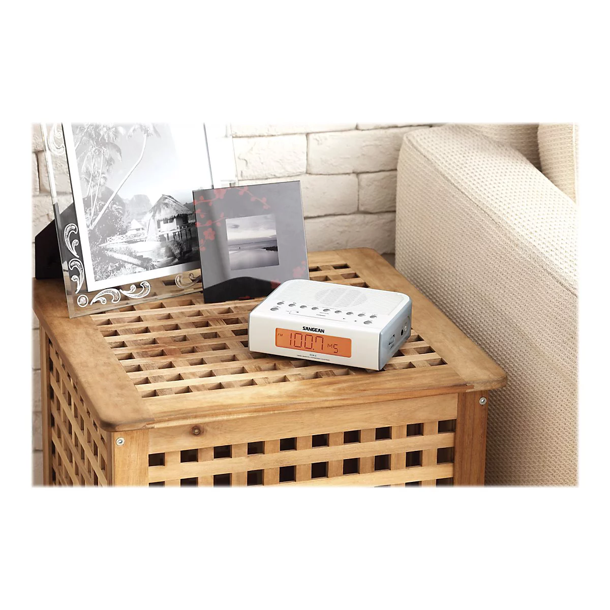 Ein weiÃŸes Digitalradio mit orangefarbener Anzeige, platziert auf einem Holztisch. Im Hintergrund: Fotos und eine Couch.