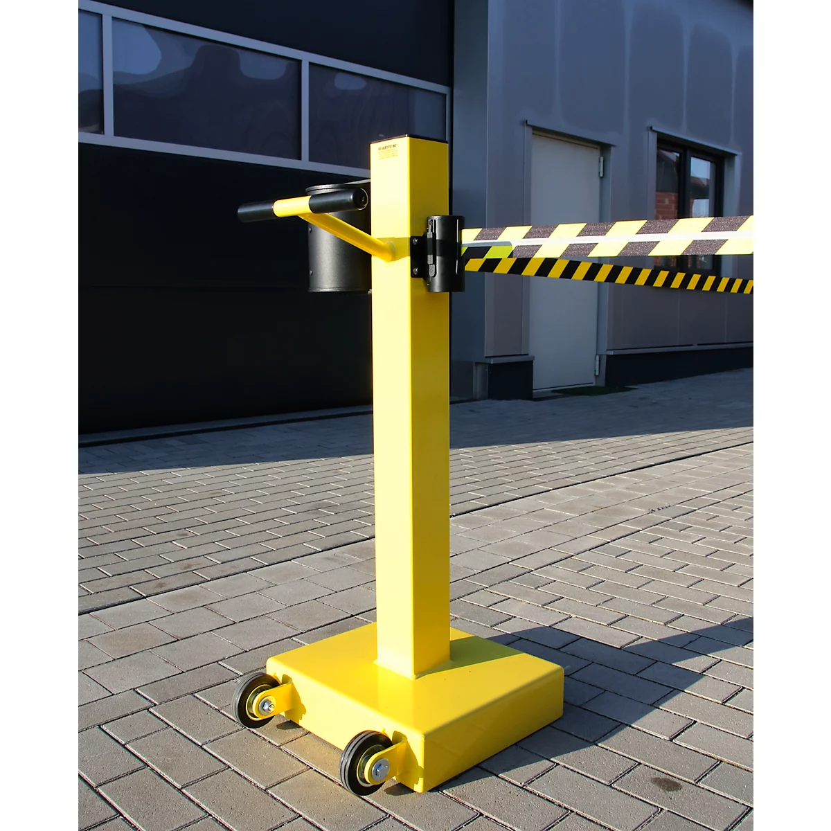 Barrière mobile jaune avec ruban d'avertissement noir et jaune ; se dresse sur des pavés.