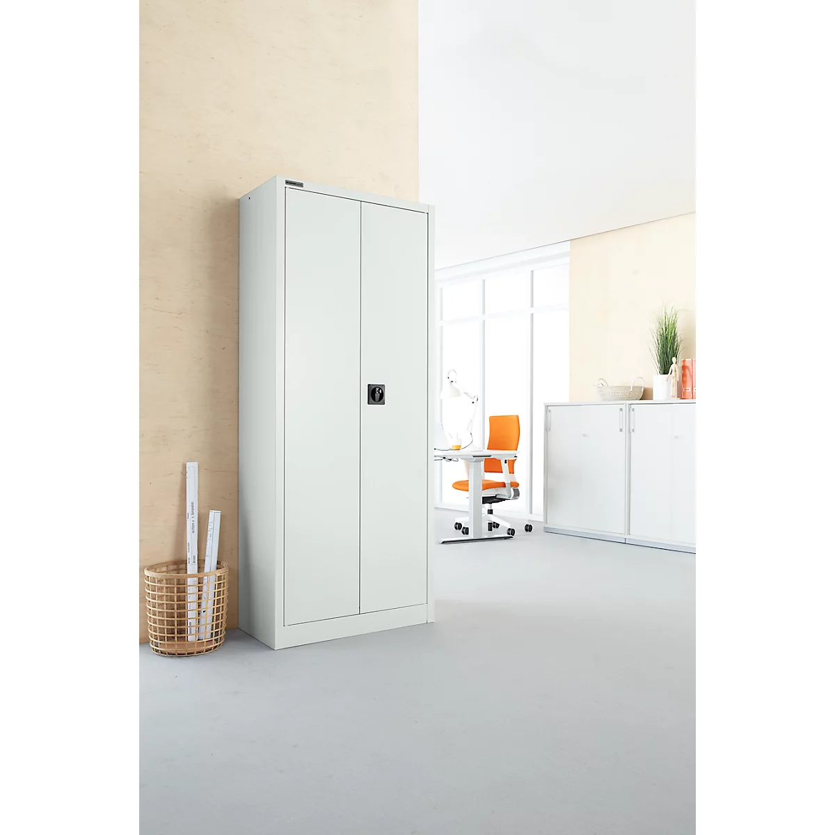 Armoire en acier blanc à deux portes dans un bureau. En arrière-plan, une table avec une chaise.