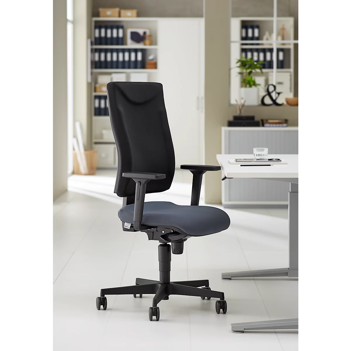 Chaise de bureau noire sur fond clair. La chaise a un dossier haut, des accoudoirs et une base roulante.