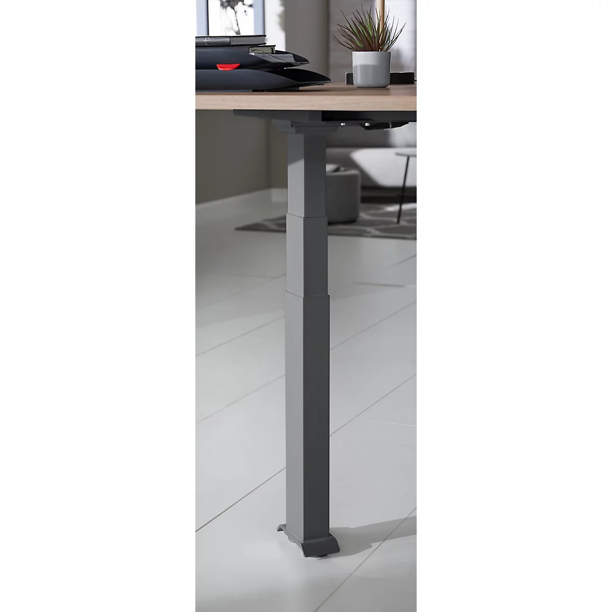 Grey, height-adjustable metal desk leg against a bright background.
