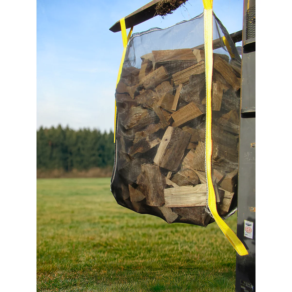 Grote zak brandhout, gele banden. Op de achtergrond weide, bos en blauwe lucht.
