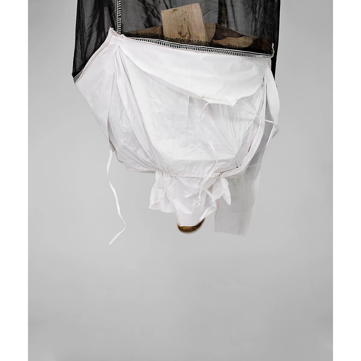 Detailopname van een witte stoffen tas bevestigd aan een zwart net. Bovenop een stuk hout.