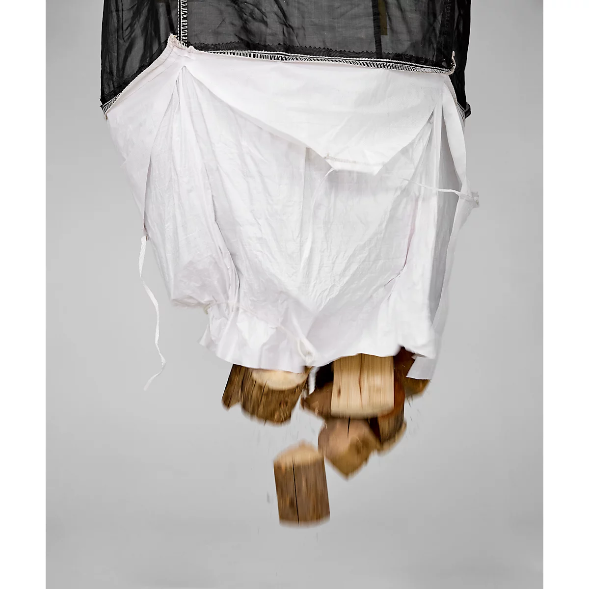 Van bovenaf vallen stukken hout uit een witte en zwarte stoffen zak. De achtergrond is grijs.