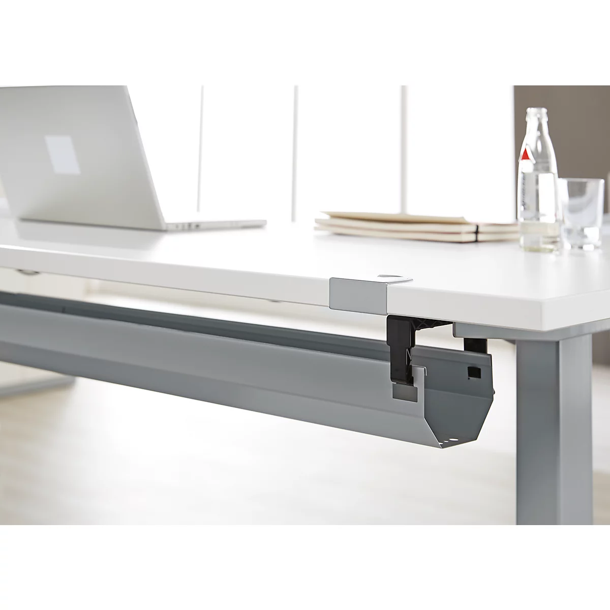Witte bureau met laptop, waterfles, glazen en grijze kabelgoot.