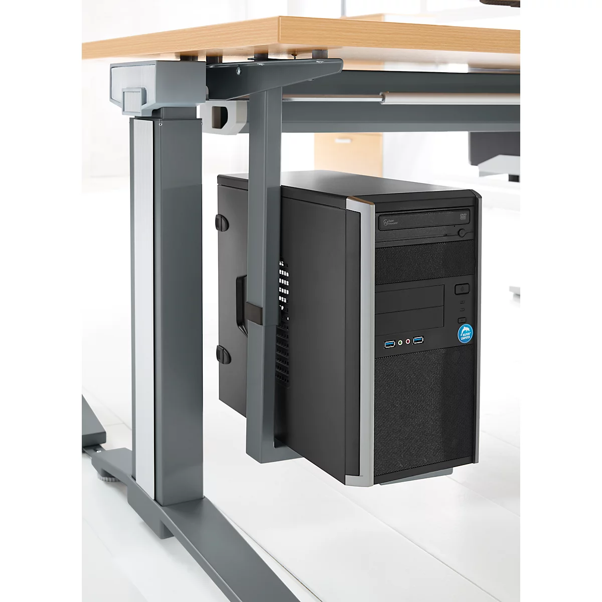 Zwarte pc, gemonteerd onder een in hoogte verstelbaar bureau. De pc-houder is grijs. Het bureau heeft een houten blad.