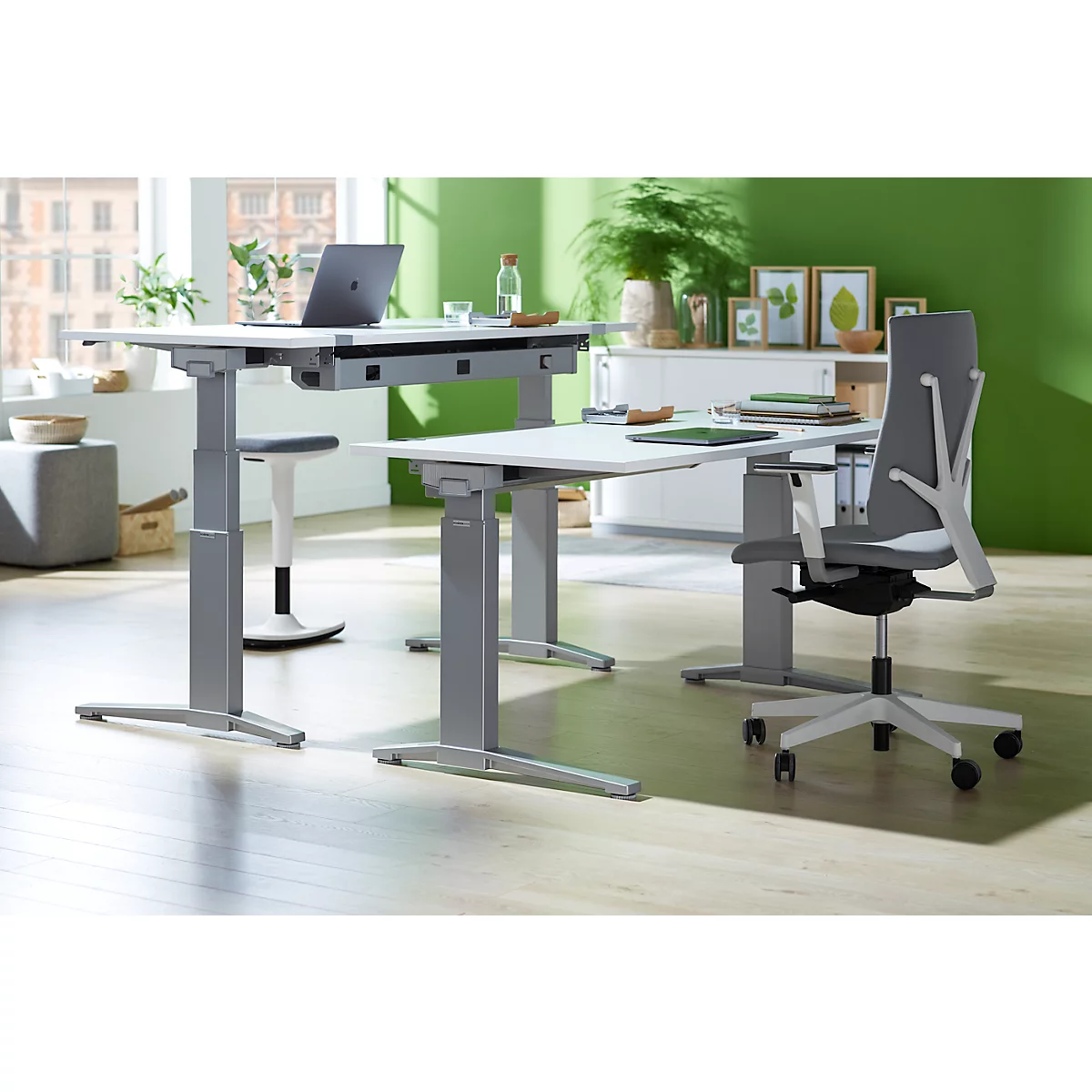 Two height-adjustable desks in a modern office. A laptop sits on the table. Ergonomic office chair.