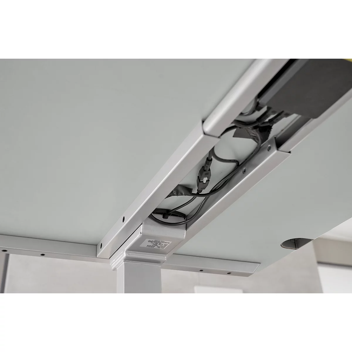 Close-up of the underside of a desk with cable management. Gray table top with integrated cable tray, cables and power supply.