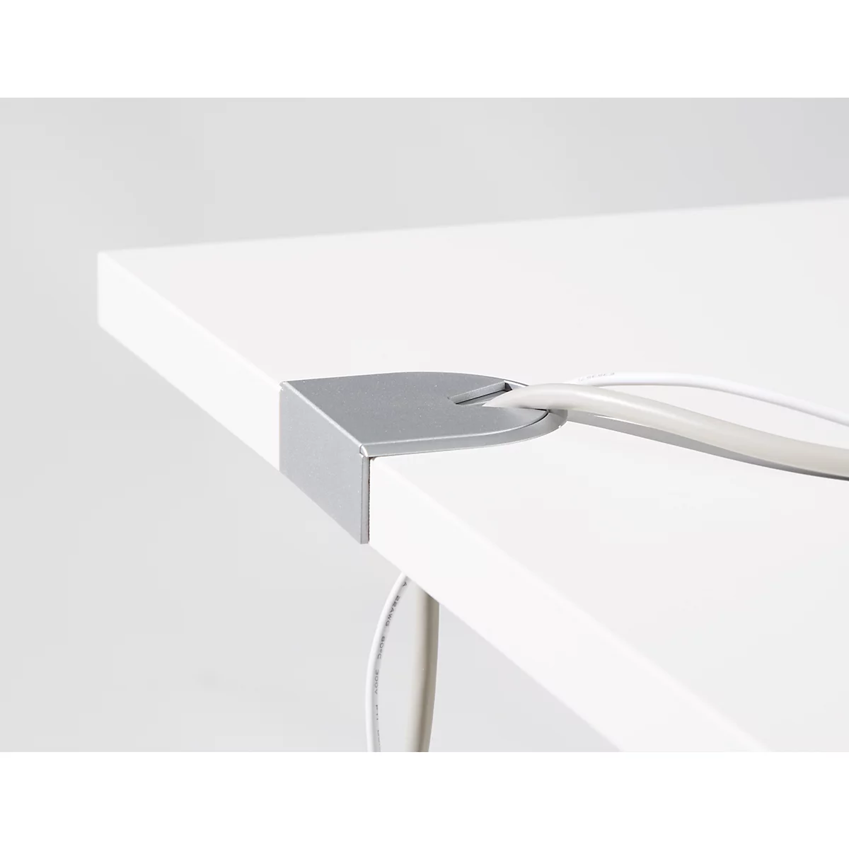 Corner of a white desk with a metal cable grommet. White cables run through it.
