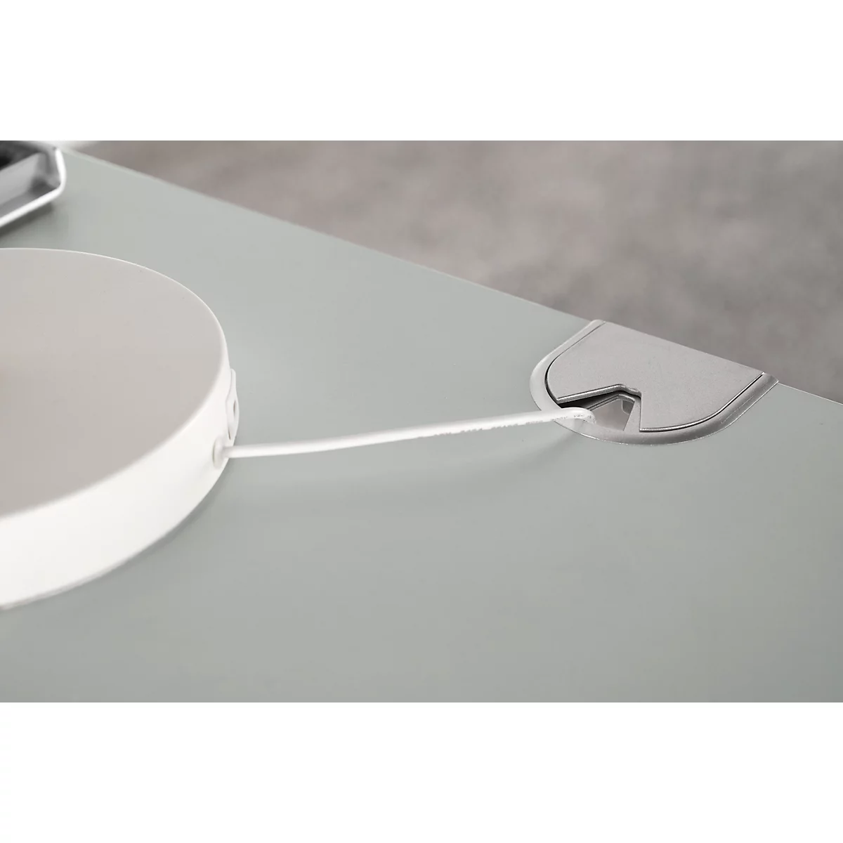 Close-up of a grey desk with a white cable and a cable grommet.