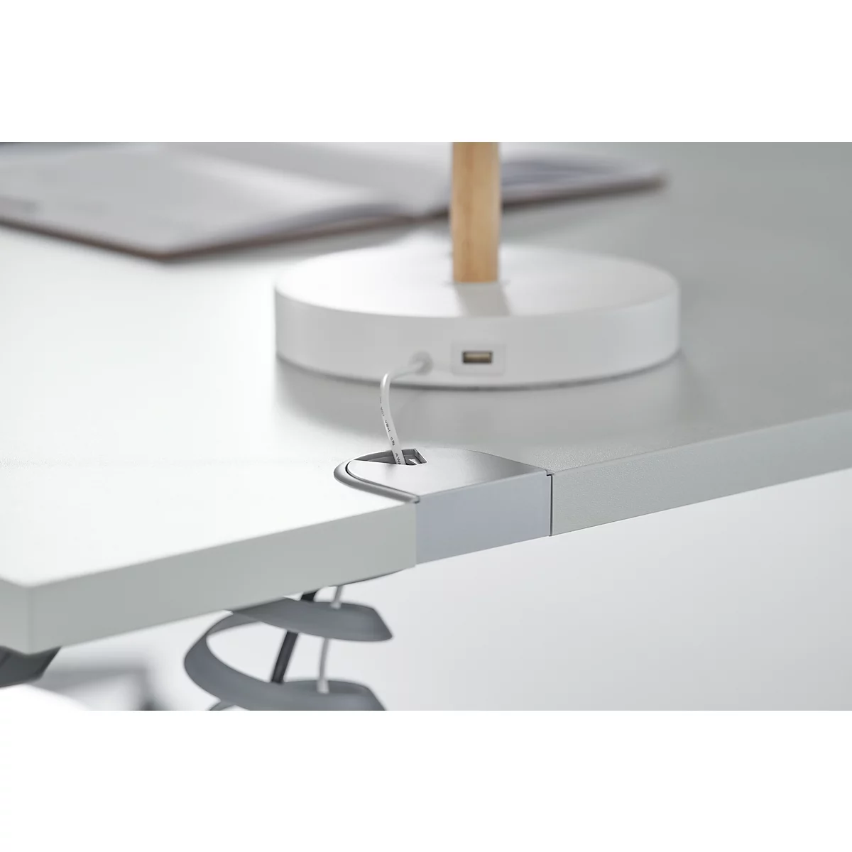 Detail of a tabletop with integrated cable holder, above a desk lamp.