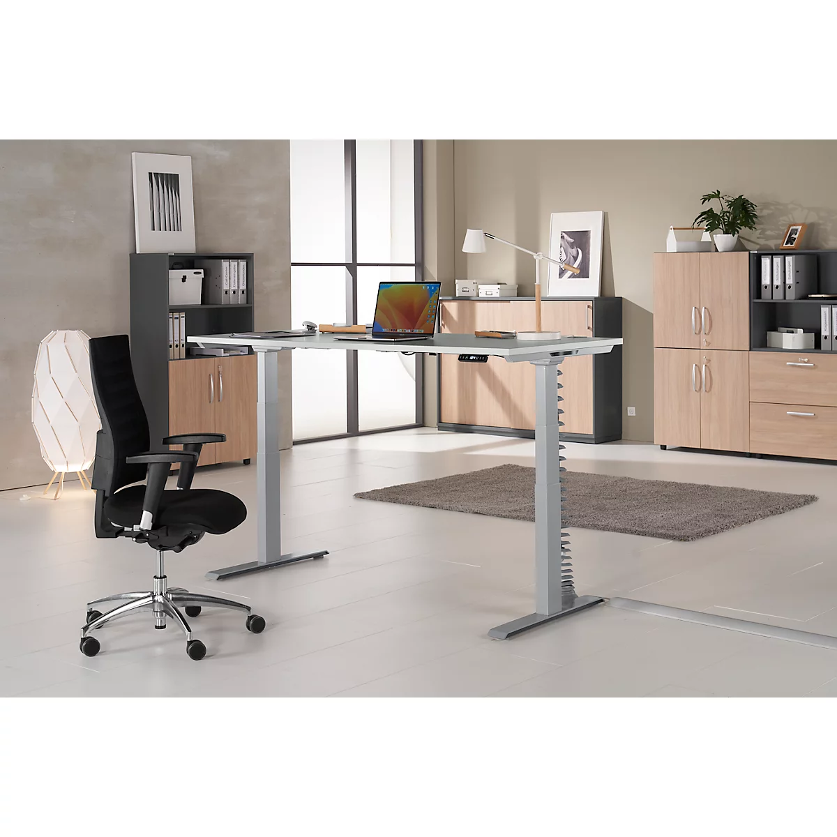 Office featuring a height-adjustable desk, black office chair, laptop, and furniture.