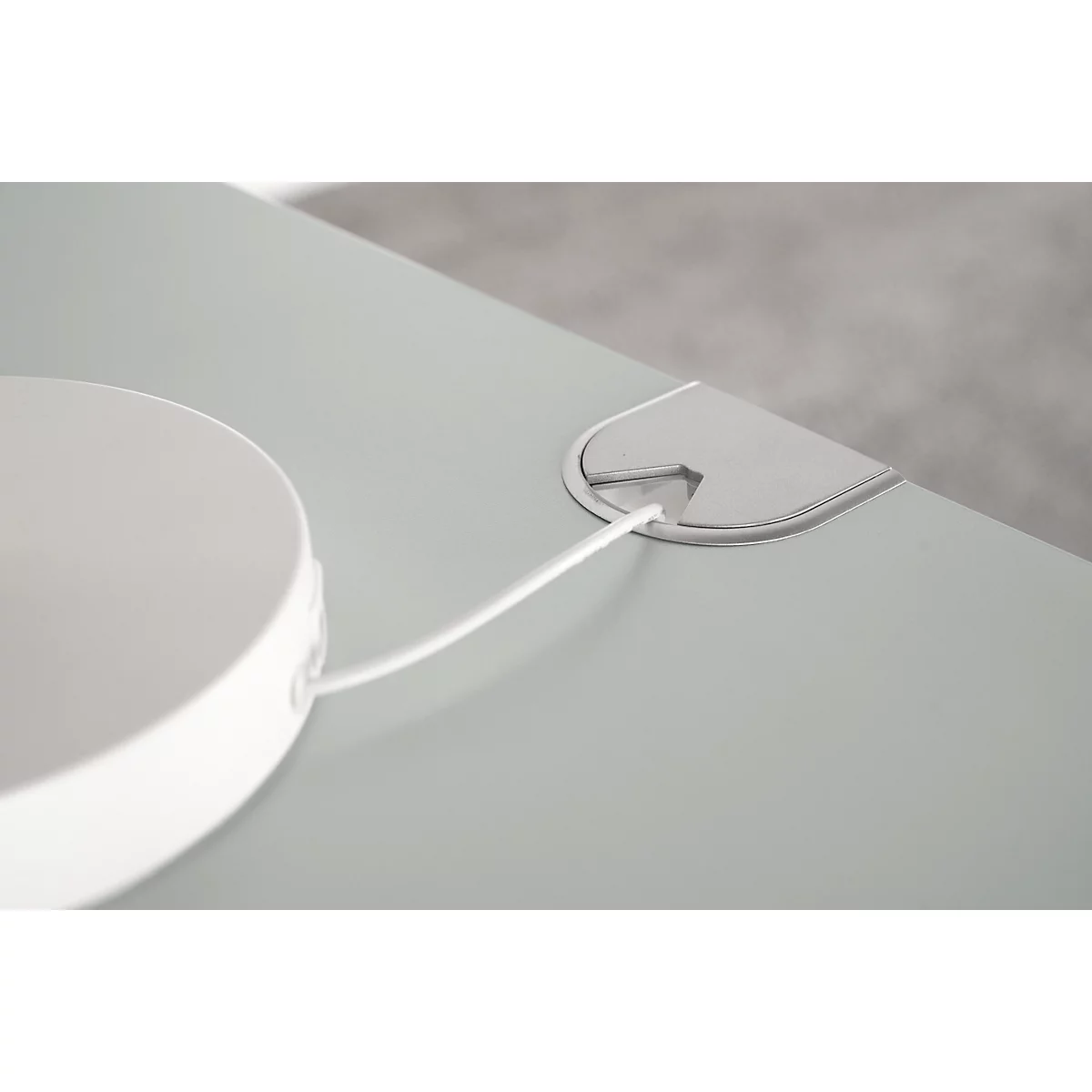 Close-up: White round object with cable leading through a table opening.