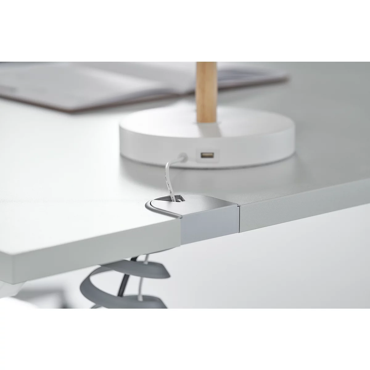 Close-up of a grey desk with an integrated power outlet and cable holder.