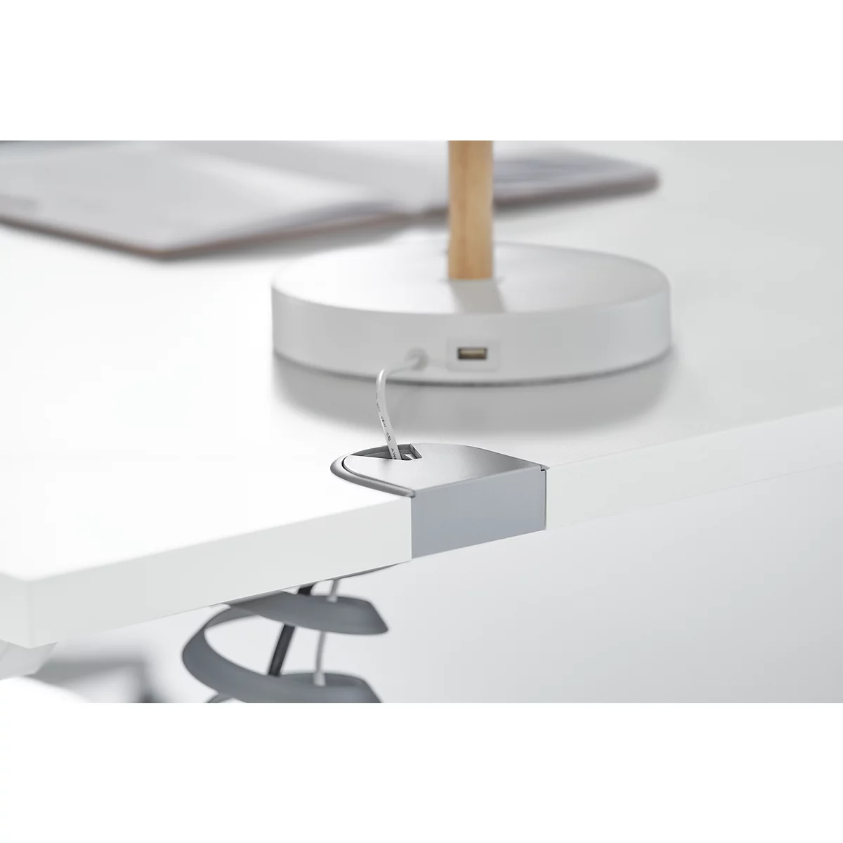 Close-up of a white desk clamp with a gray lamp attached. The base of the lamp with a USB port is visible in the background.