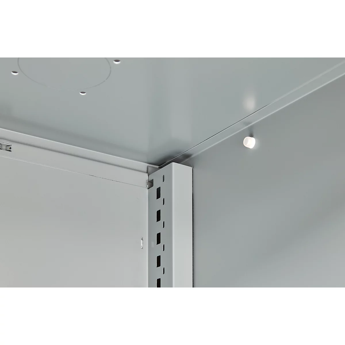 Close-up of a grey metal construction. The corner of a housing with shelf brackets and lighting is visible.