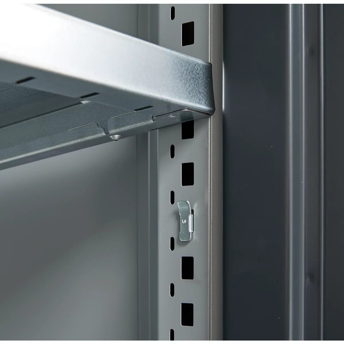 Close-up of a metal shelf. The silver shelves are attached to a gray vertical metal post with a bracket.