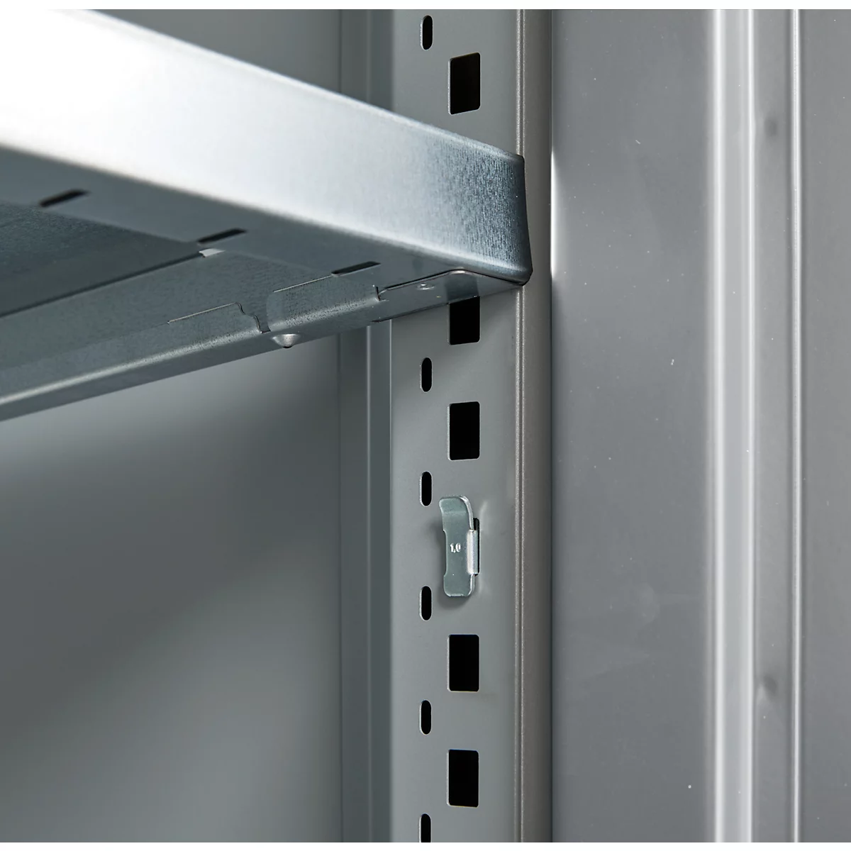Close-up of a metal shelf mounted in a light gray cabinet. The gray metal construction shows a shelf bracket.