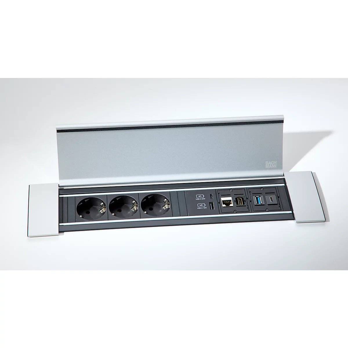 Silberne Tischanschlussbox mit drei Steckdosen, Netzwerk-, USB- und HDMI-Anschlüssen auf grauem Hintergrund.