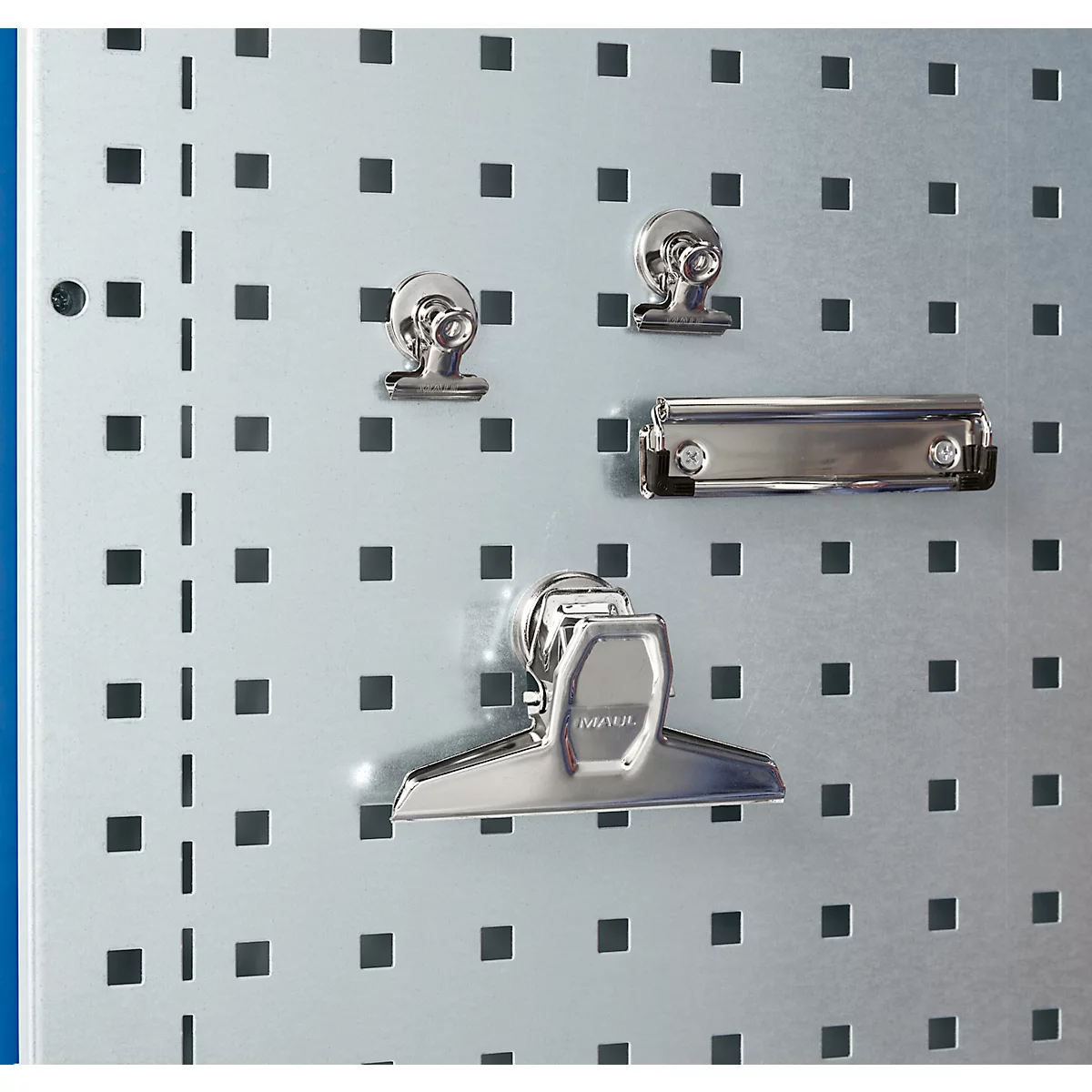 Nahaufnahme von Büroklammern und Klemmbrett an einer Metallwand mit quadratischen Löchern.