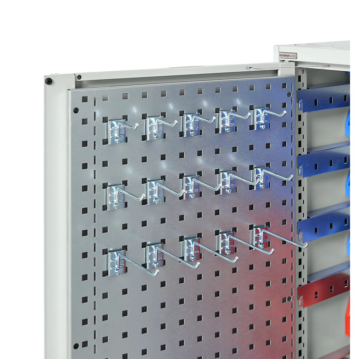 Nahaufnahme einer Lochwand mit Metallhaken, dahinter Regale in Blau und Rot.