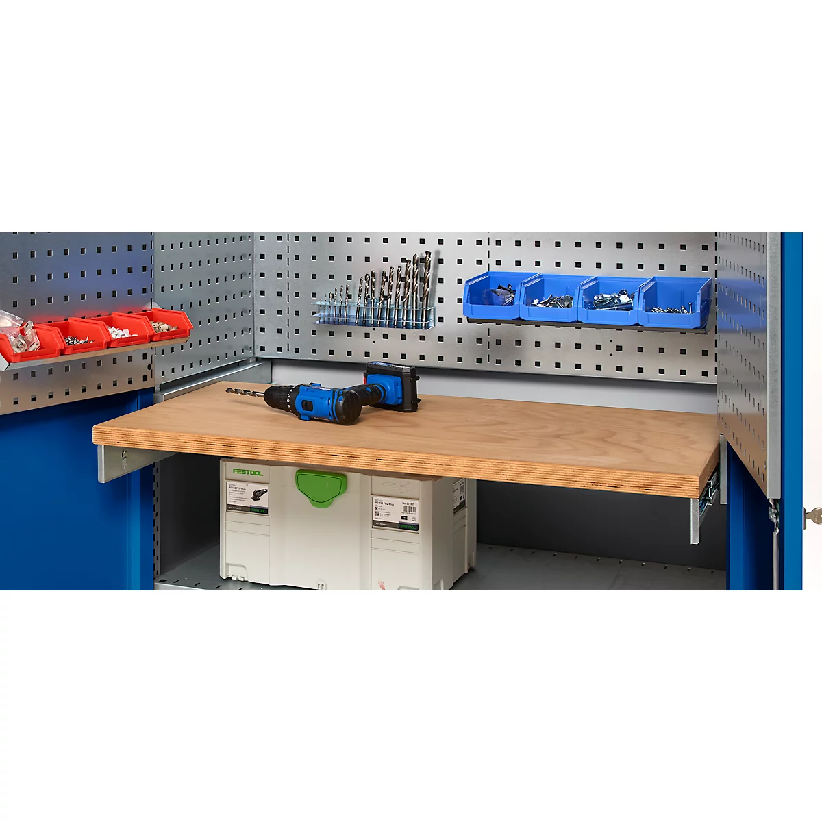 Workbench with tools and work materials. Drill, screws, etc. are on the wooden top. Background: perforated wall.