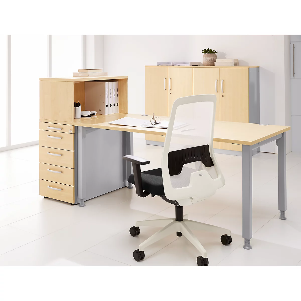 Bright office desk with white mesh office chair, file folders and cabinets in the background.