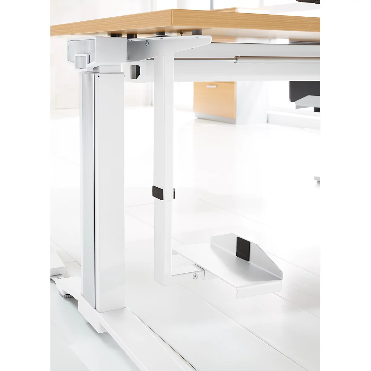 Gros plan d'un bureau réglable en hauteur avec un dessus en bois clair et un cadre blanc. Repose-pieds.