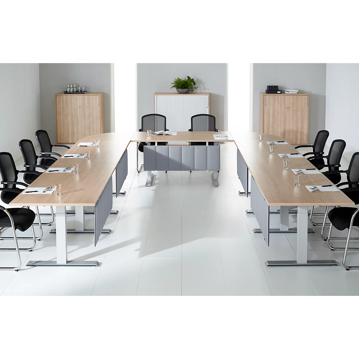 Salle de conférence avec table en forme de U, chaises et armoires. Fenêtres éclairant la pièce.