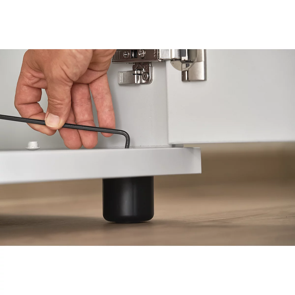 Close-up of a hand inserting an Allen wrench into a piece of furniture. Black furniture feet.