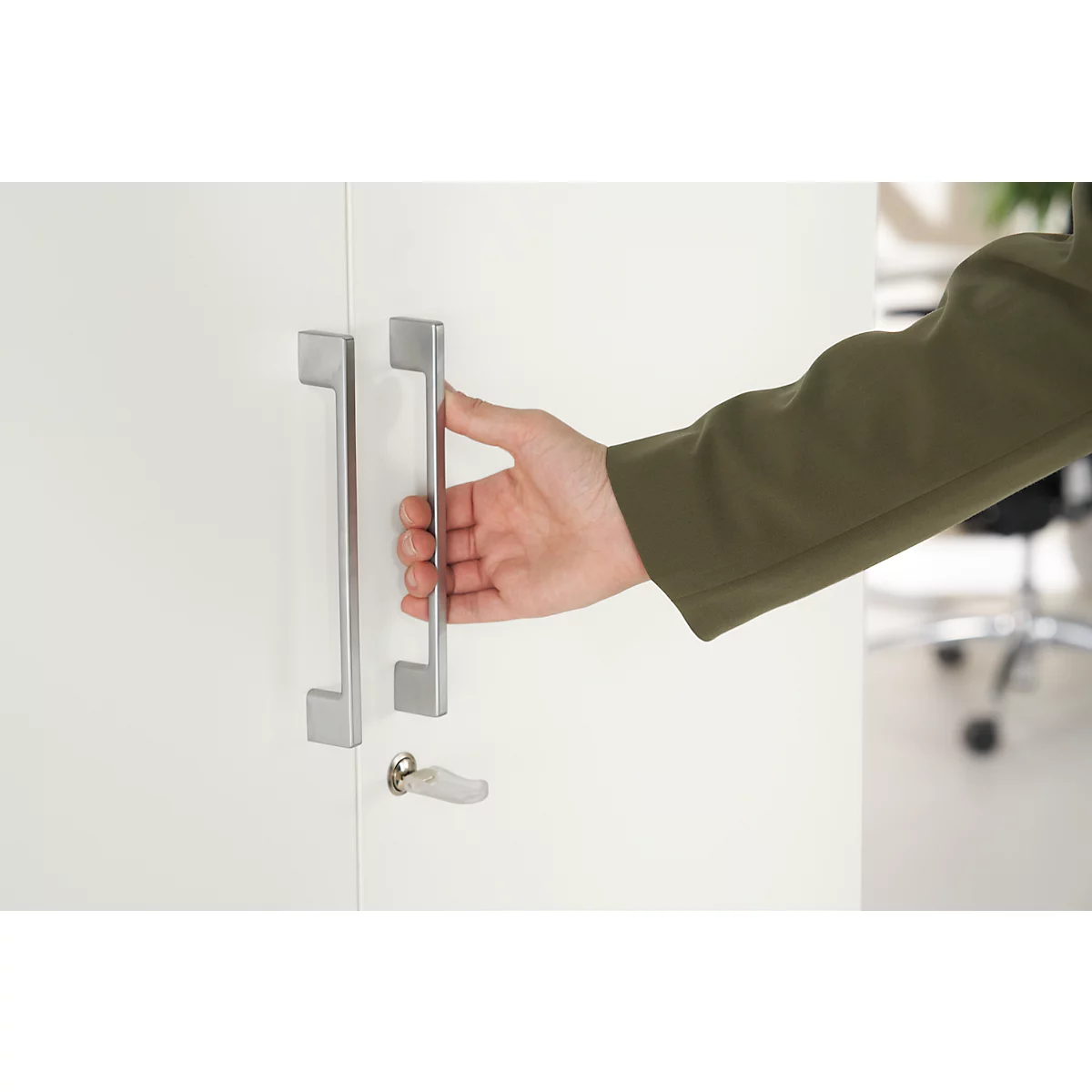 A hand opens a white cabinet door, metal handle. View into the office.