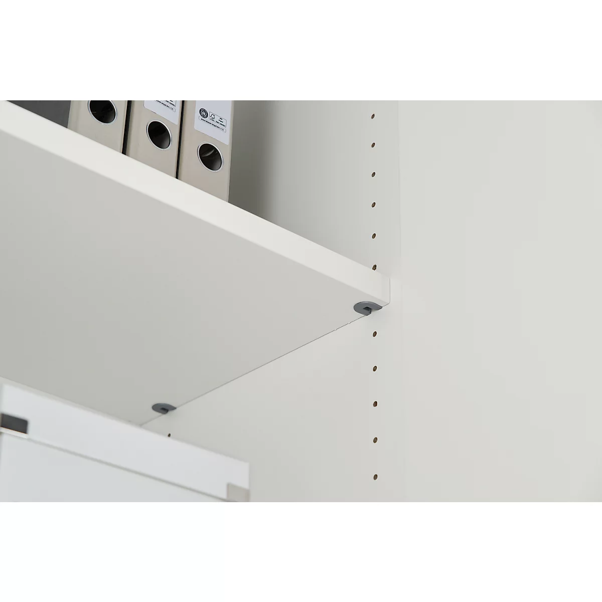 Light beige shelves with gray pins on a white wall. Folders are on the top shelf.