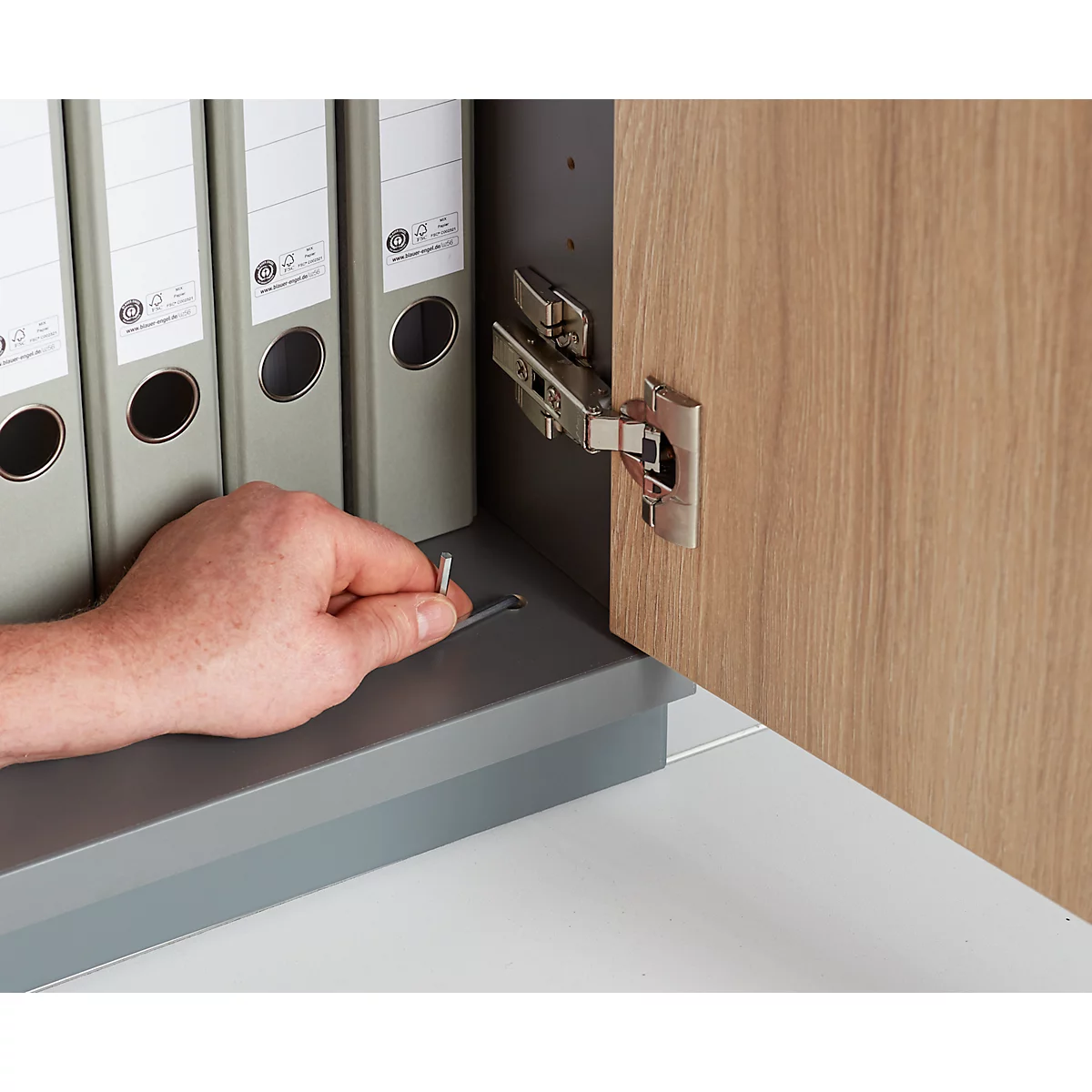 Close-up of a hand placing a pen in a cabinet. Folders are visible behind the hand.