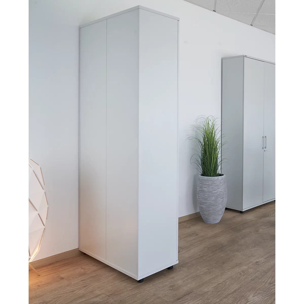 White cabinet in corner arrangement. Another cabinet on the right, with a potted plant in between on wooden flooring.