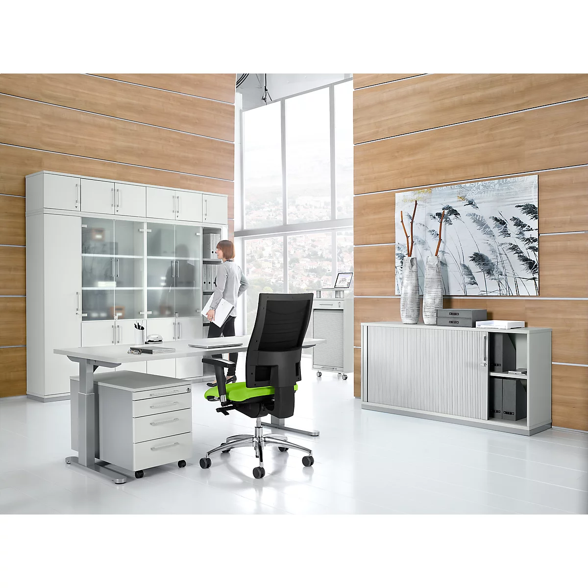 A modern office with a desk, chair and cabinets. A person stands at the window.