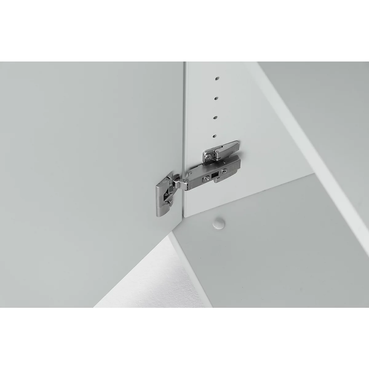 Close-up of a metallic hinge attached to a white cabinet door. Other cabinet parts are visible in the background.