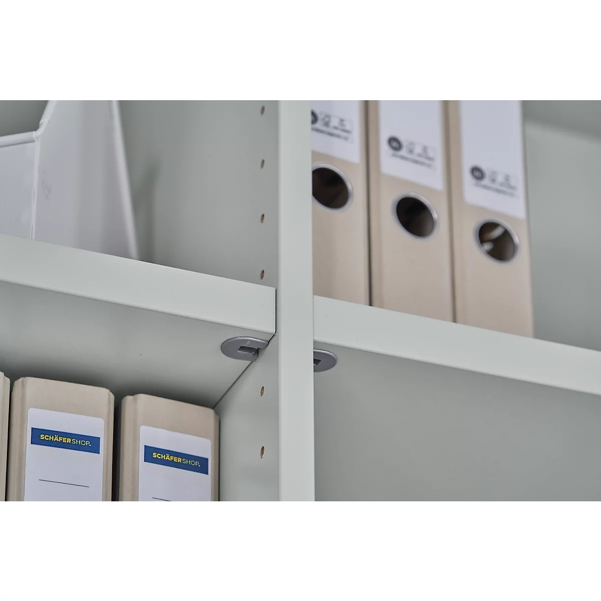 Close-up of a light grey shelf with file folders. The words "Schäfer Shop" can be read on the folders.