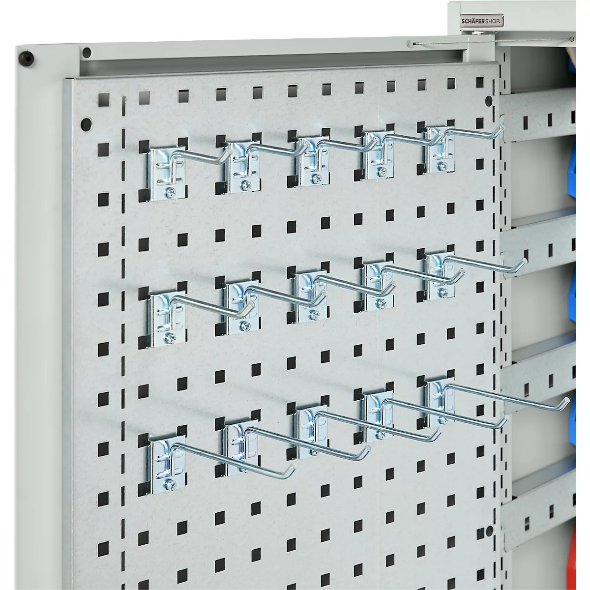 Metalen geperforeerd paneel met haken, daarachter een plank met gekleurde mappen.