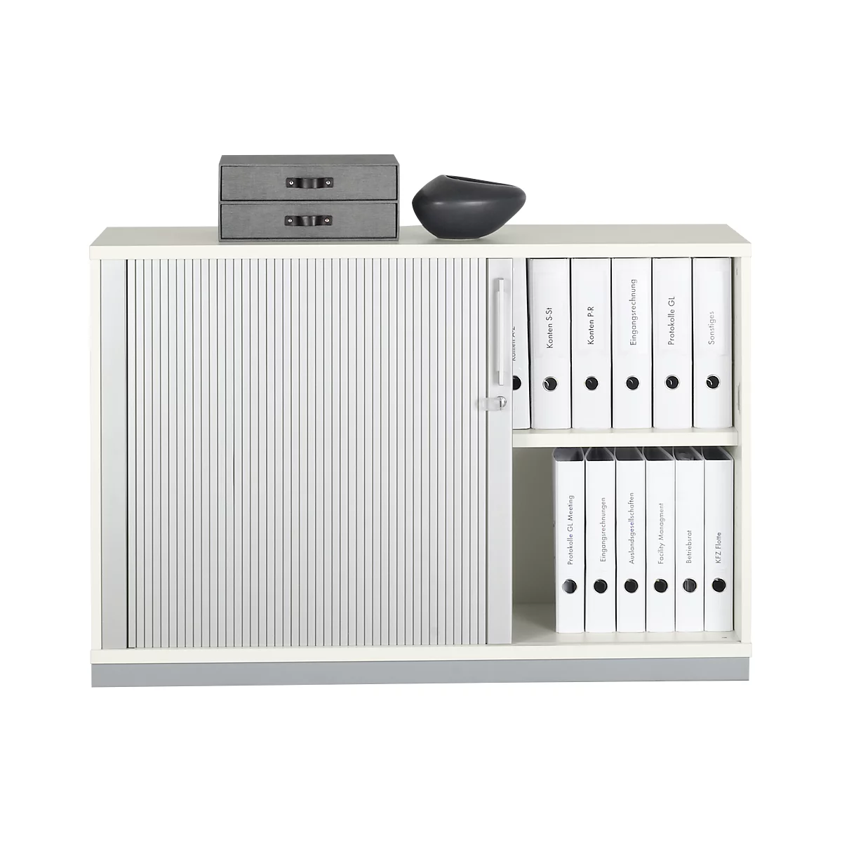 White cabinet with roller shutter, grey drawers and black vase. Open compartments with white binders.