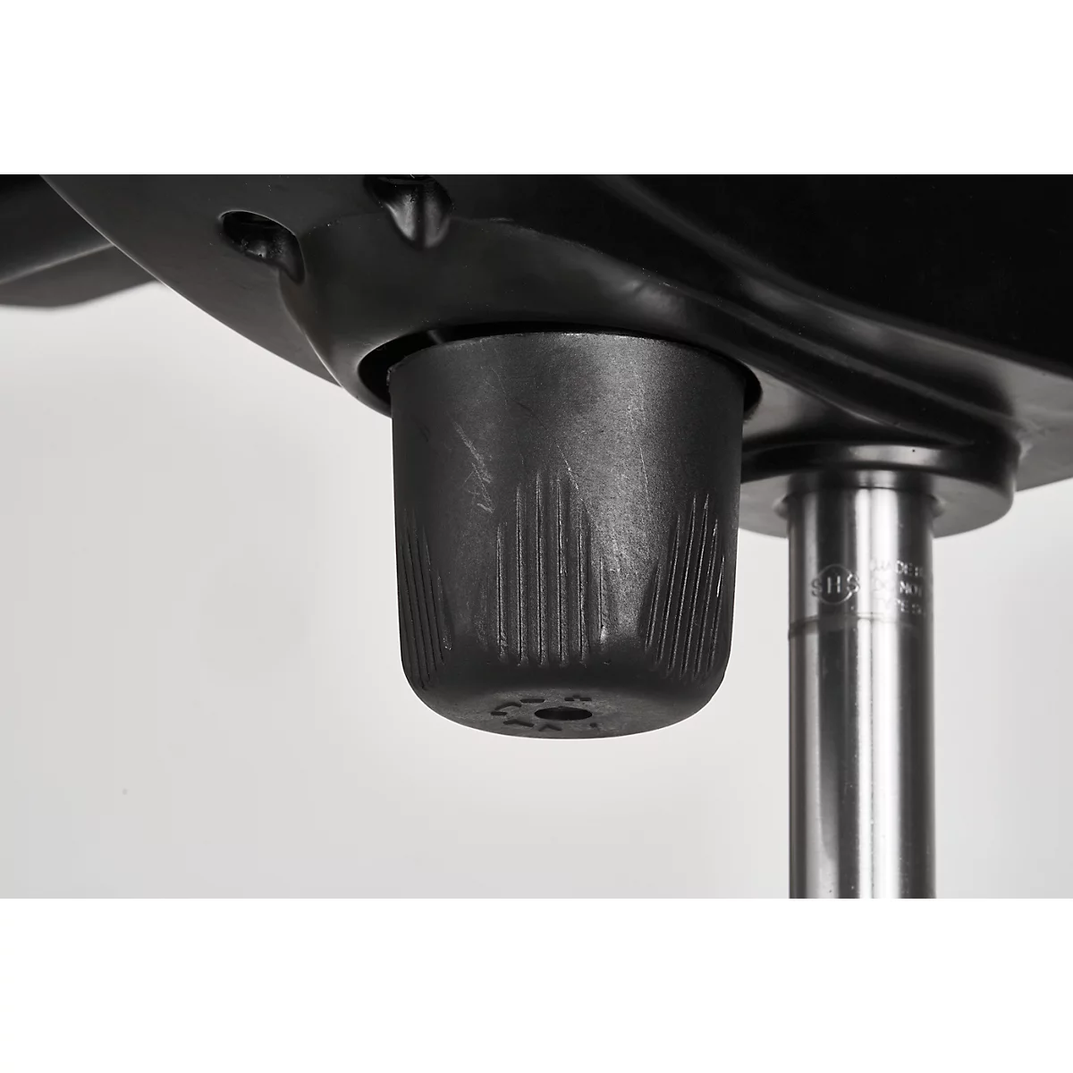 Close-up of the underside of a chair. A cylindrical, ribbed element surrounds a metal tube.