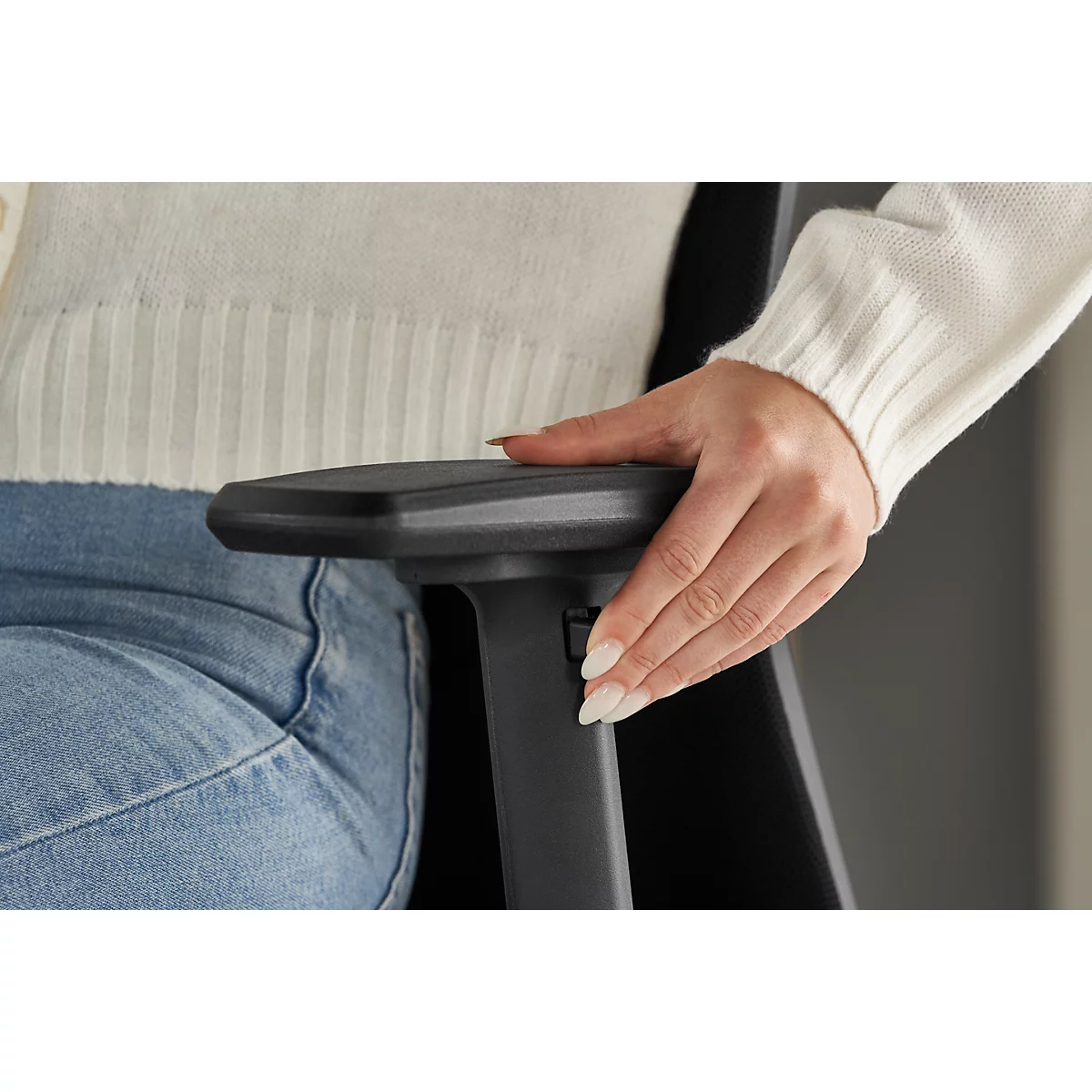 Close-up of a hand on an armrest, pressing a button. The person wears a white sweater and jeans.