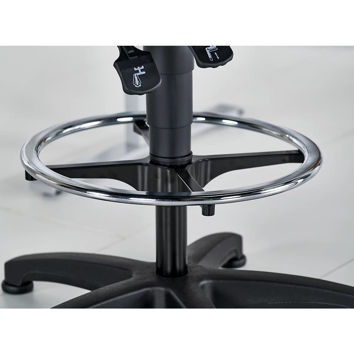 Detailaufnahme eines schwarzen Bürostuhls mit Fußstütze. Verchromte Fußstütze und schwarzes Gestell. Hebel und Beschriftungen.