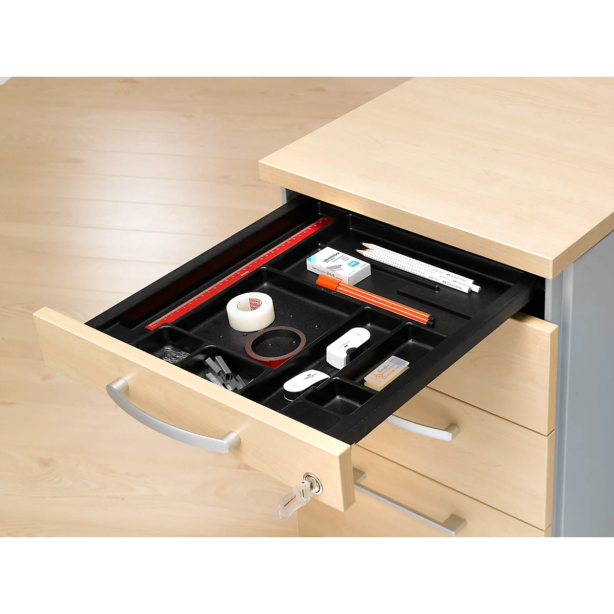 Tiroir de bureau ouvert avec fournitures de bureau : ruban adhésif, stylos, règle, gomme.