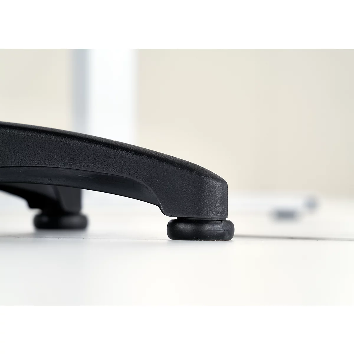 Gros plan du train d'atterrissage d'une chaise de bureau noire. Deux pieds ronds reposent sur la surface blanche.