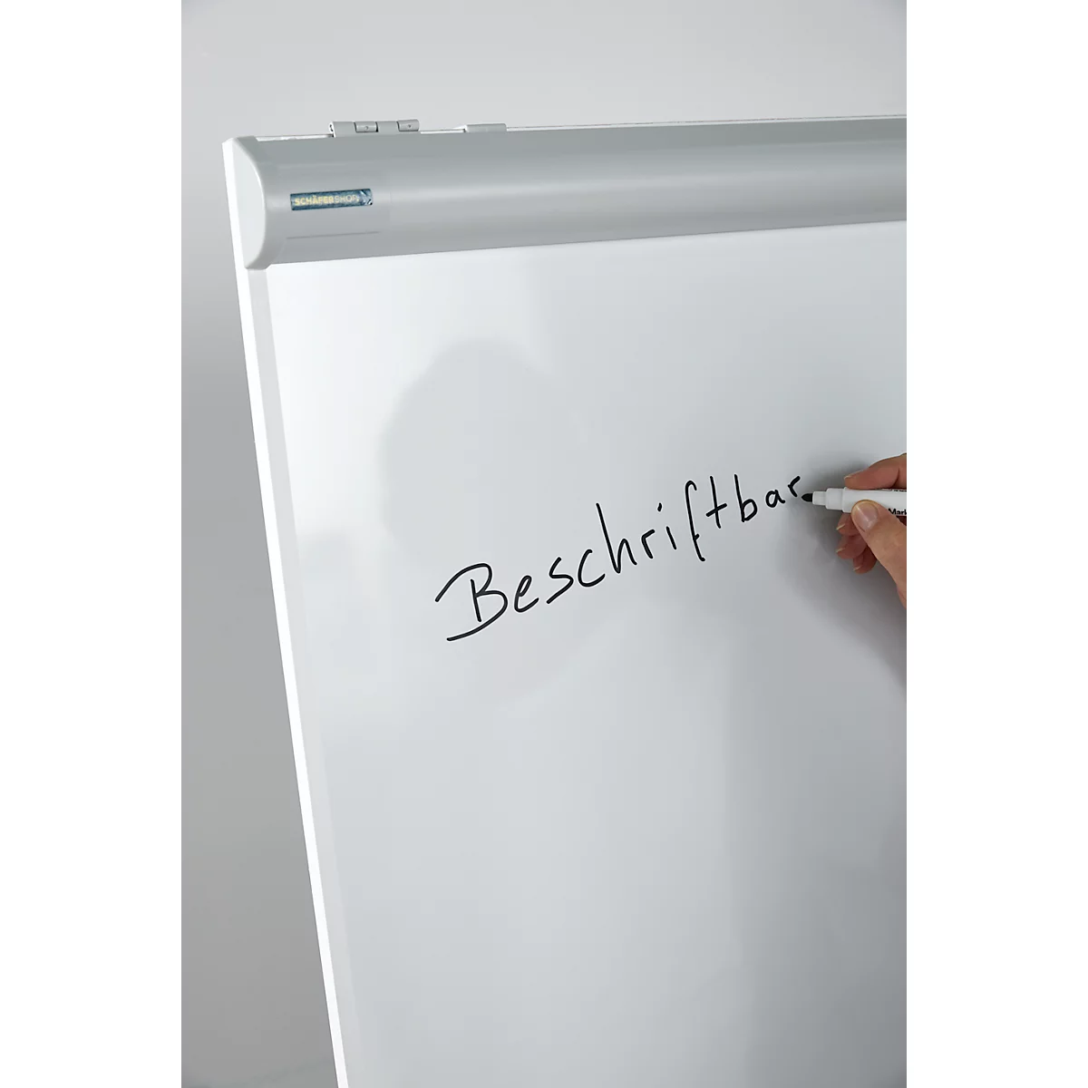 White flip chart with the inscription "Beschriftbar". A hand writes on the board with a black pen.